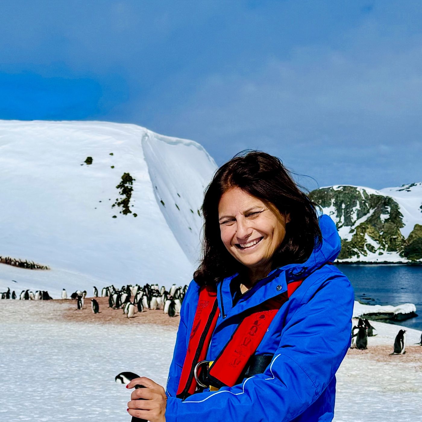 Periodista sonriendo con pingüinos en la Antártida.