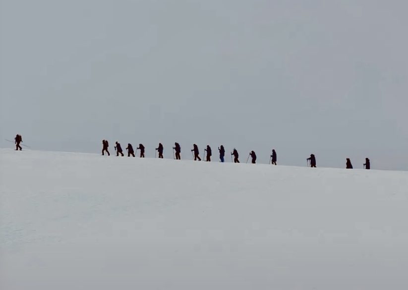 Grupo de viajeros caminando en fila por un paisaje nevado durante un desembarco en la Antártida.